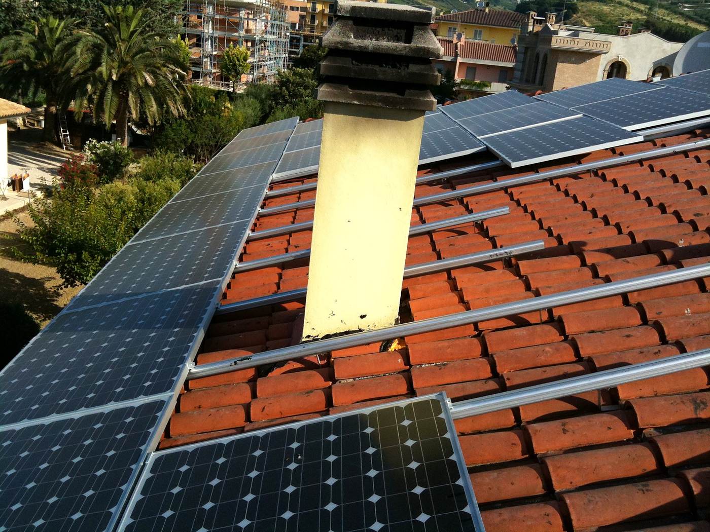 Binari di montaggio fotovoltaico posati a ridosso di un camino su tetto in coppi
