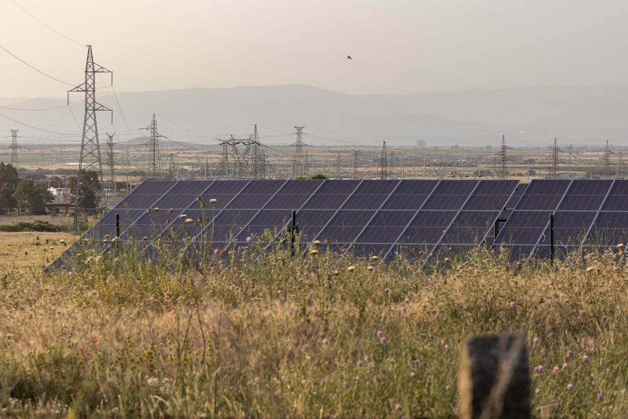 Impianto fotovoltaico a terra con erba alta, vicino a linee elettriche di alta tensione