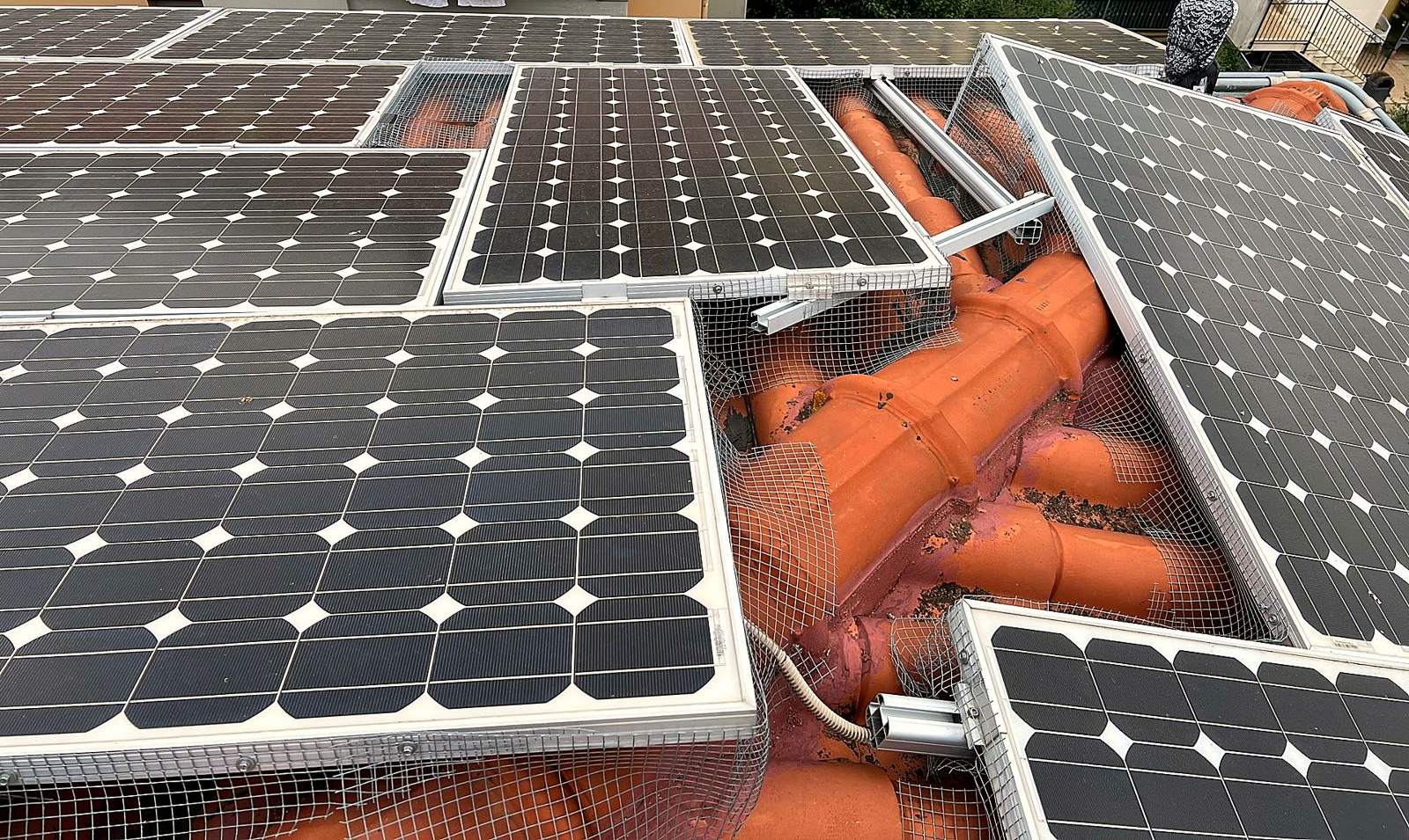 Impianto fotovoltaico installato male: moduli storti a cavallo del colmo, binari sporgenti e rete anti-piccioni aperta su un tetto in coppi