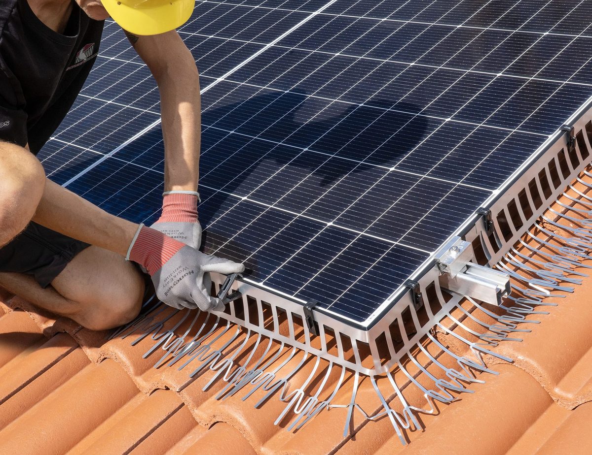 Tecnico con guanti installa la barriera anti-piccioni sull'angolo di un campo fotovoltaico su coppi