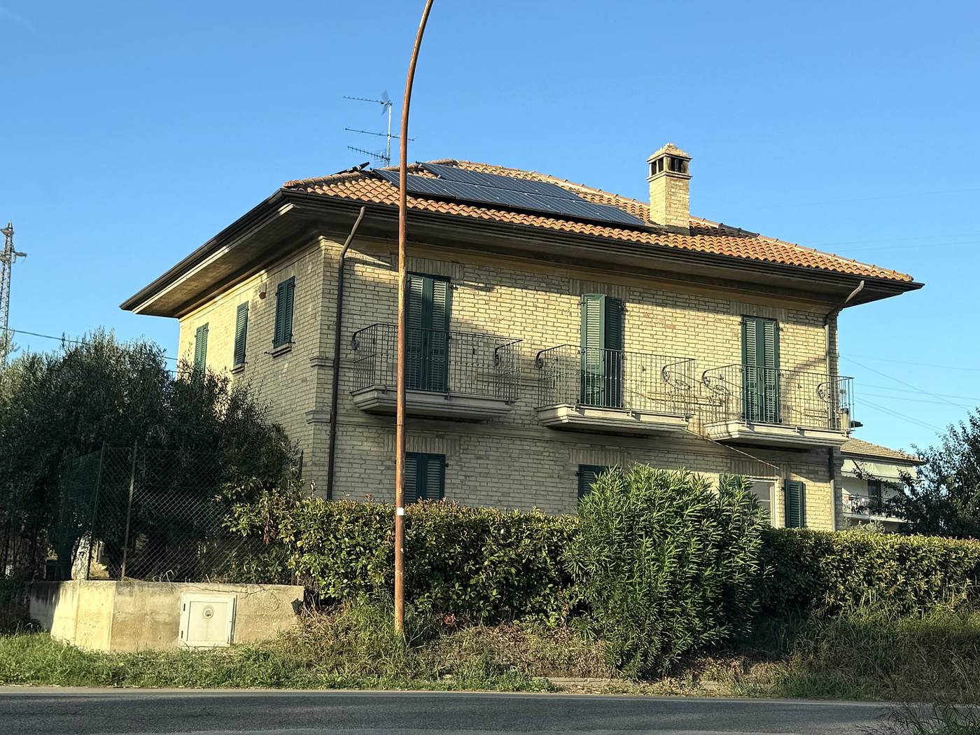 Casa in mattoni con tetto a padiglione in coppi e impianto fotovoltaico montato in modo scorretto, vista dalla strada