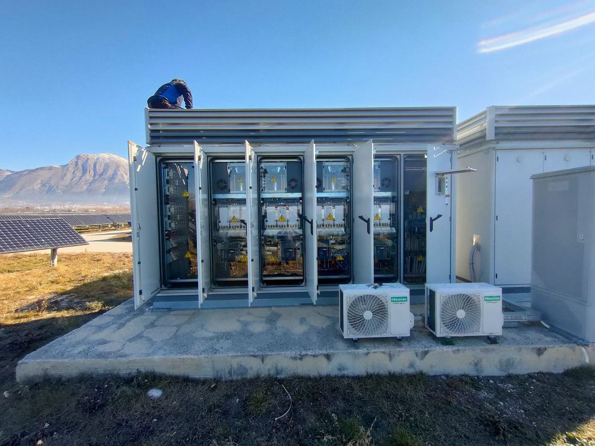 Cabine inverter centralizzati di un impianto fotovoltaico a terra con montagne sullo sfondo