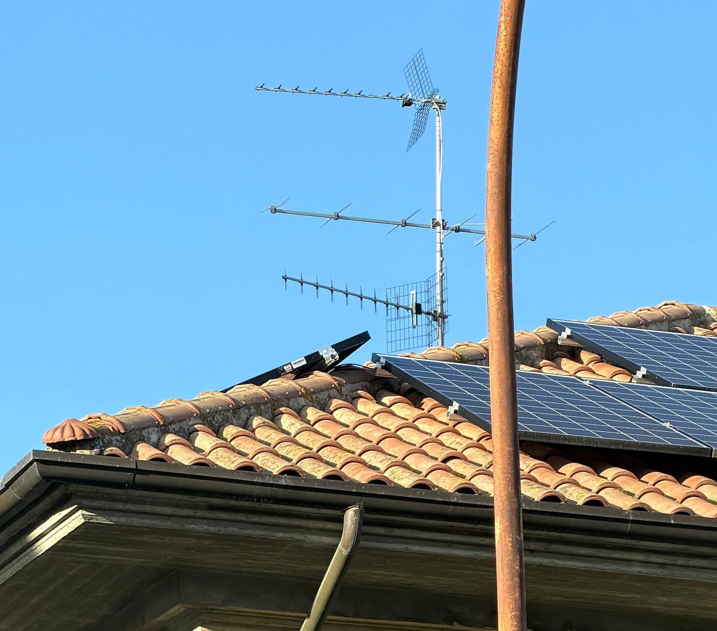 Modulo fotovoltaico sollevato e sporgente sopra il displuvio di un tetto in coppi, accanto alle antenne