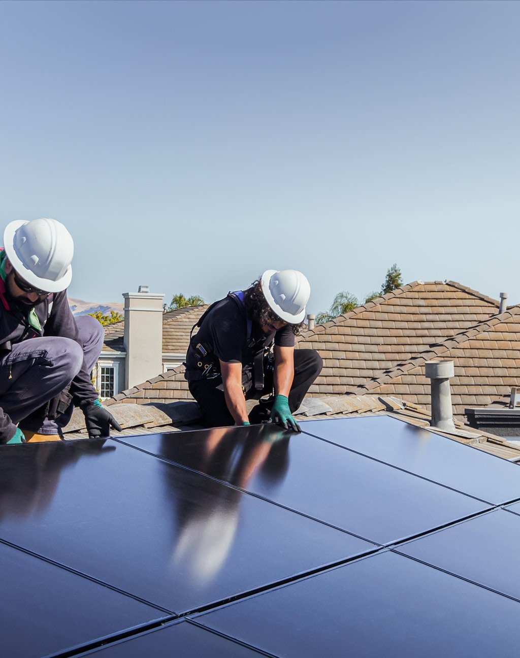 Due installatori con casco posano i moduli di un impianto fotovoltaico sul tetto