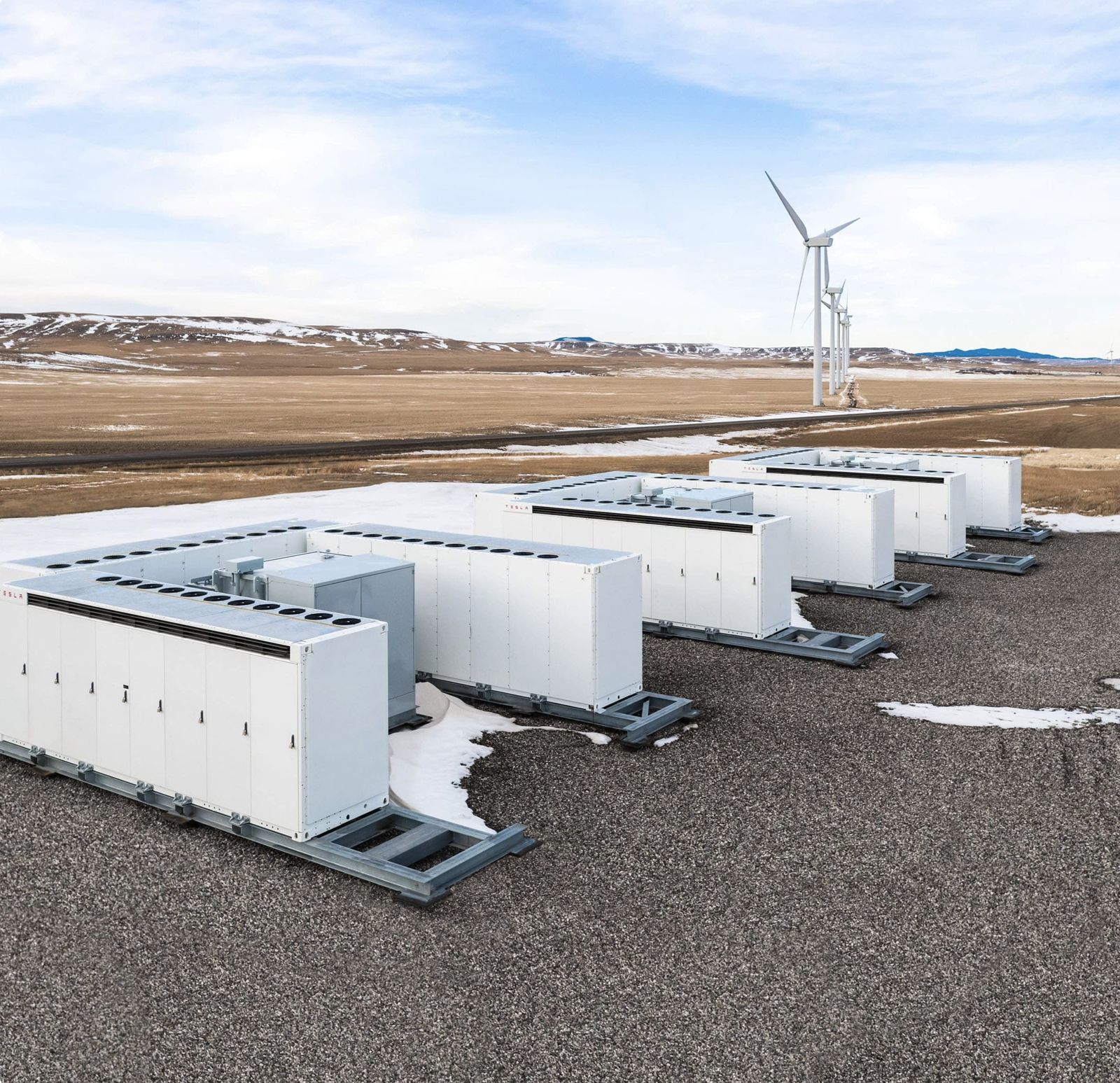 Unità Tesla Megapack in fila con una pala eolica sullo sfondo