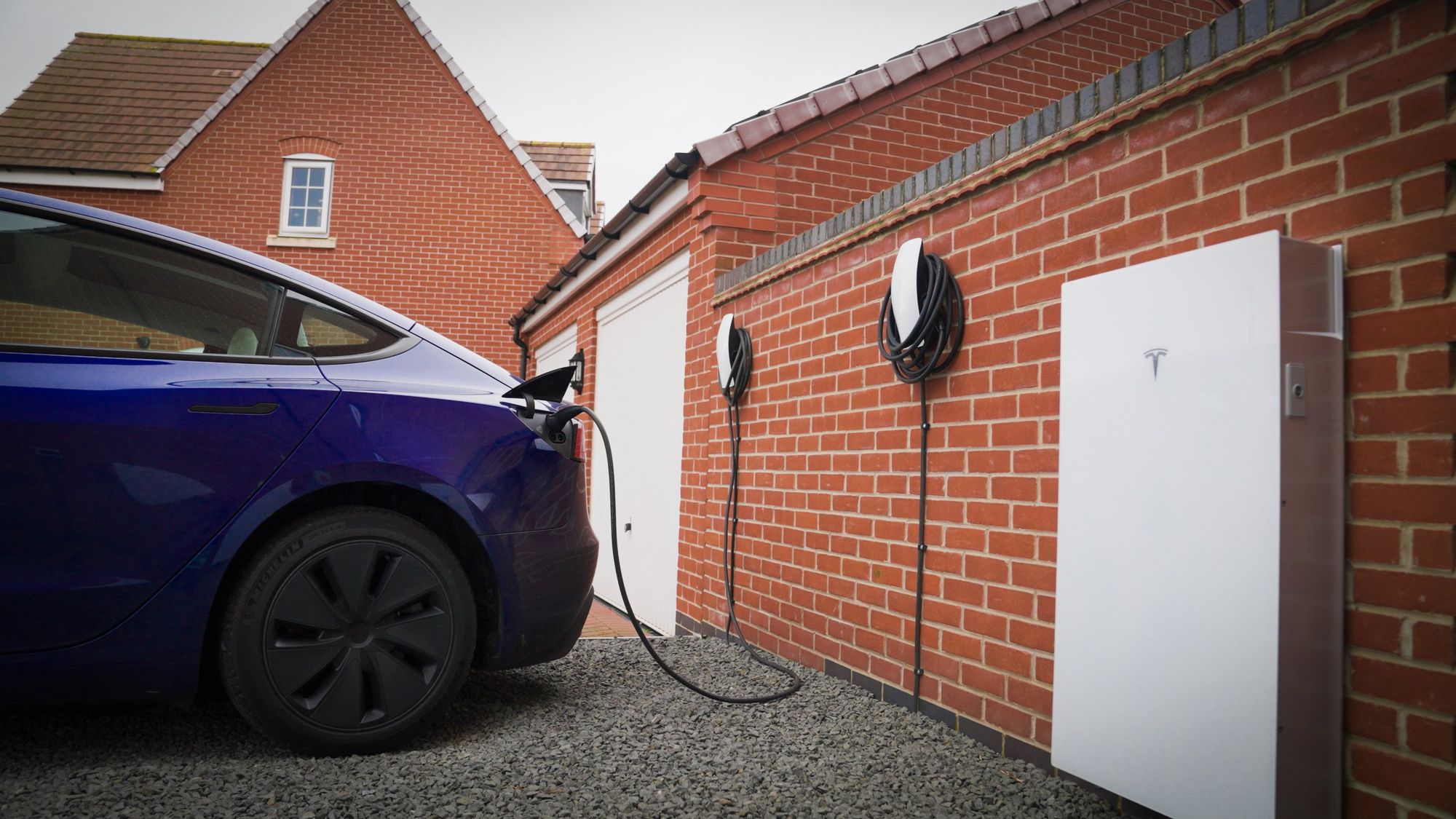 Auto Tesla in ricarica accanto a una Powerwall su un muro di mattoni