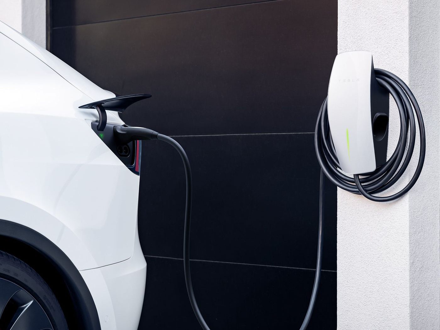 Auto elettrica in ricarica a una wallbox a parete accanto al garage